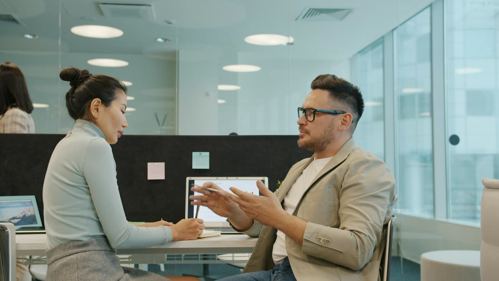 Two colleagues in conversation in a glass-walled office